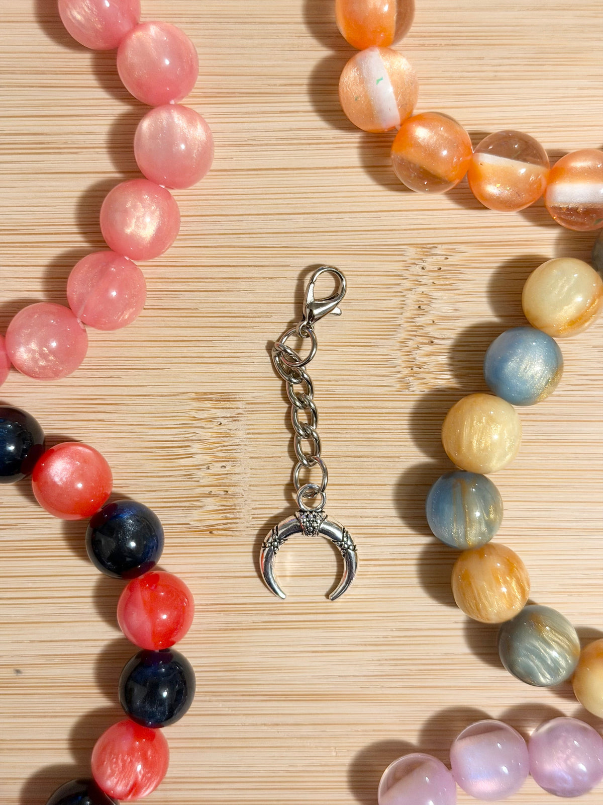 Antique silver crescent horn charm with floral detailing on a lobster clasp chain, surrounded by colorful beaded bracelets on a wooden surface