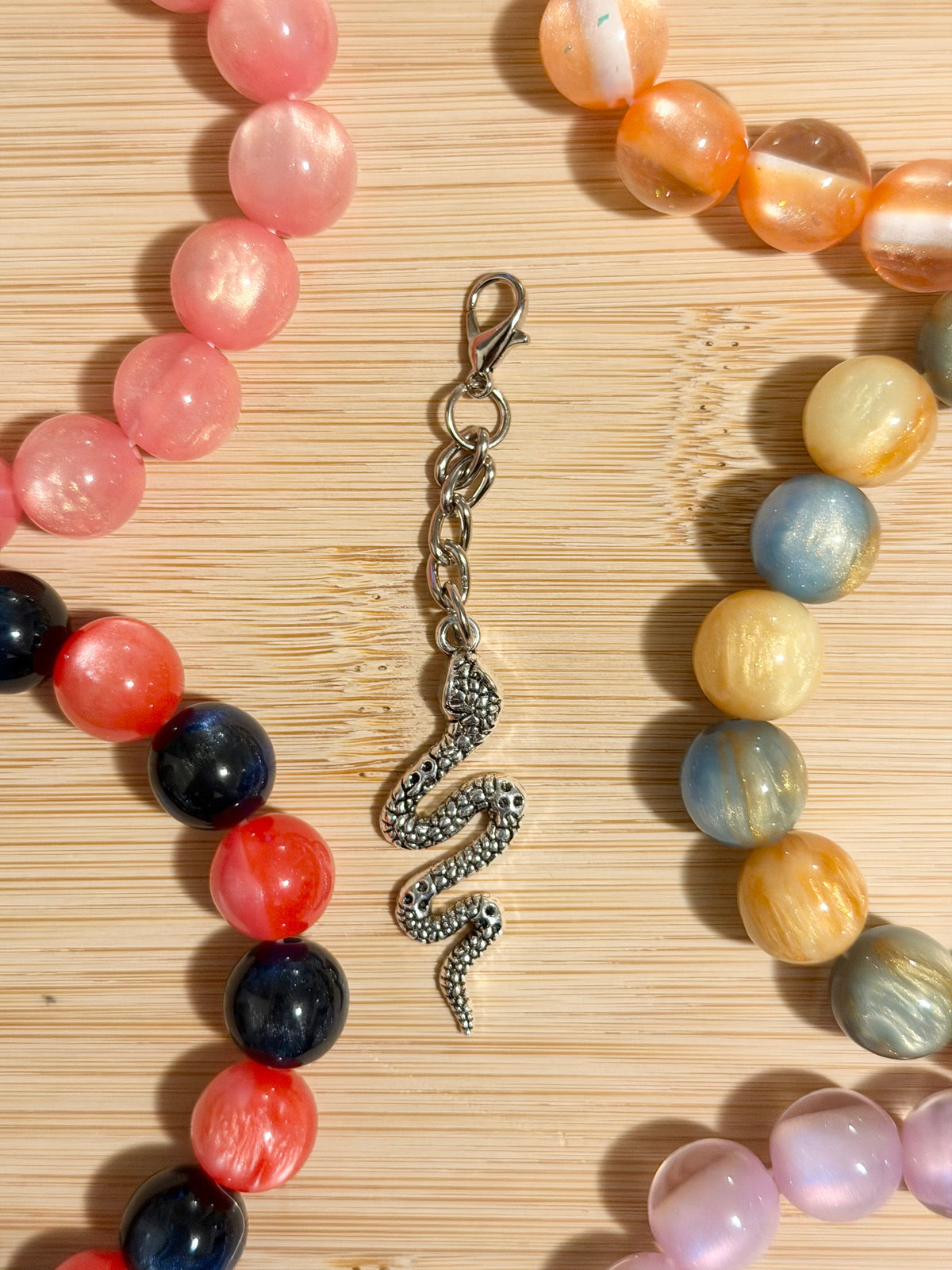 White enamel sakura cherry blossom charm on a silver lobster clasp chain, surrounded by colorful beaded bracelets on a wooden surface