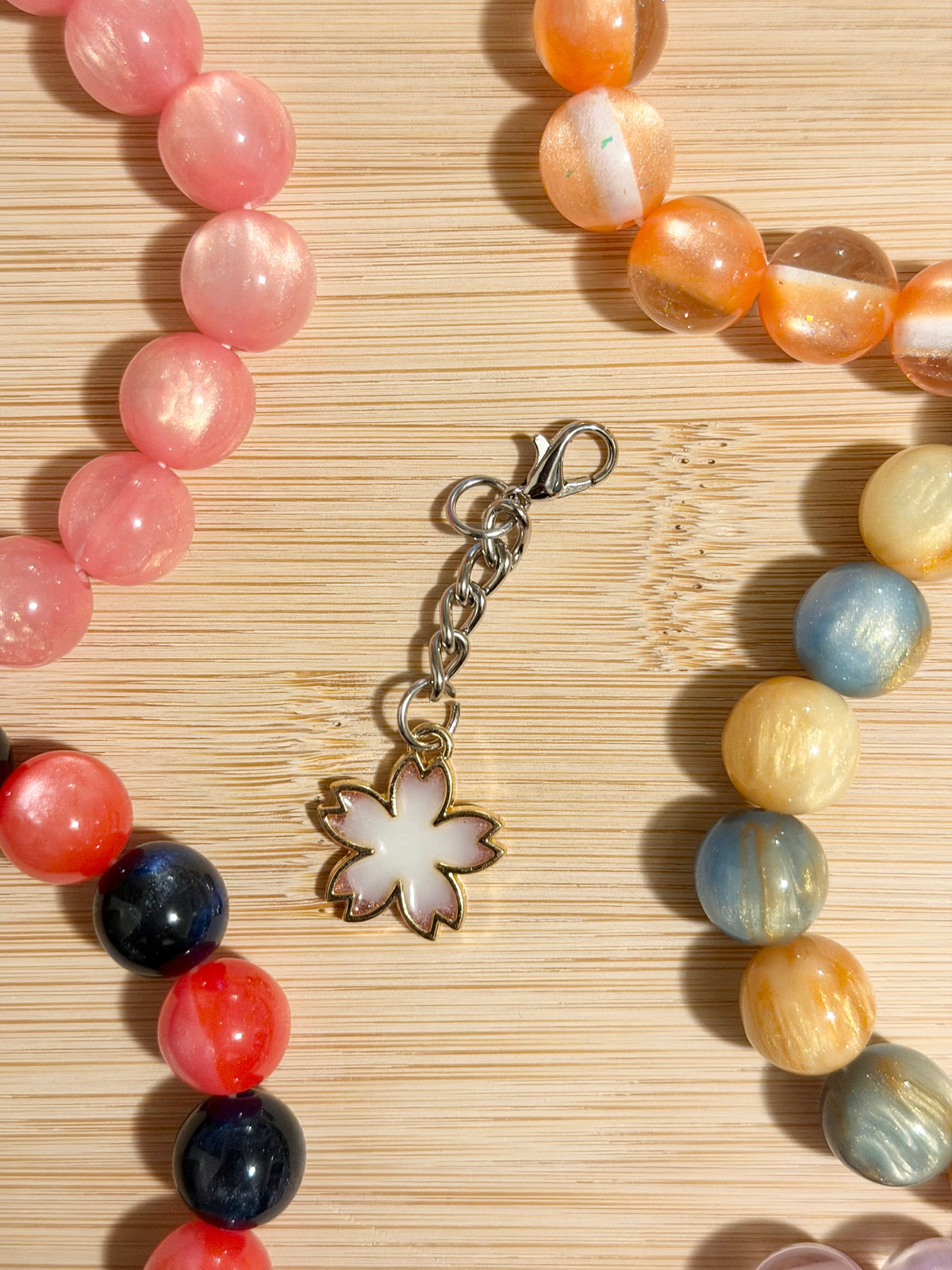 Detailed antique silver coiled snake charm on a lobster clasp chain, surrounded by colorful beaded bracelets on a wooden surface